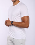 A man wearing a white short-sleeve athletic t-shirt and light gray sweatpants, shown from the waist up against a light gray studio background.