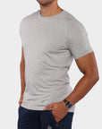 A man wearing a light gray heather crew-neck t-shirt and navy blue pants, shown from the chin down against a light gray background.