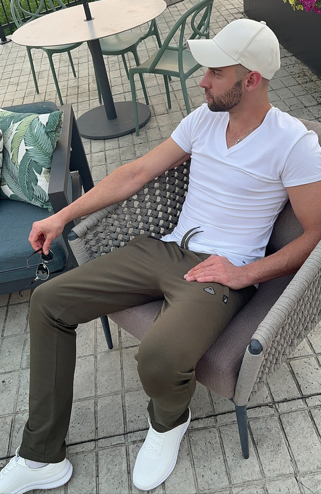 tall male model  sitting outdoors wearing khaki green long-inseam lounge pants and white t-shirt and sneakers, lifestyle view