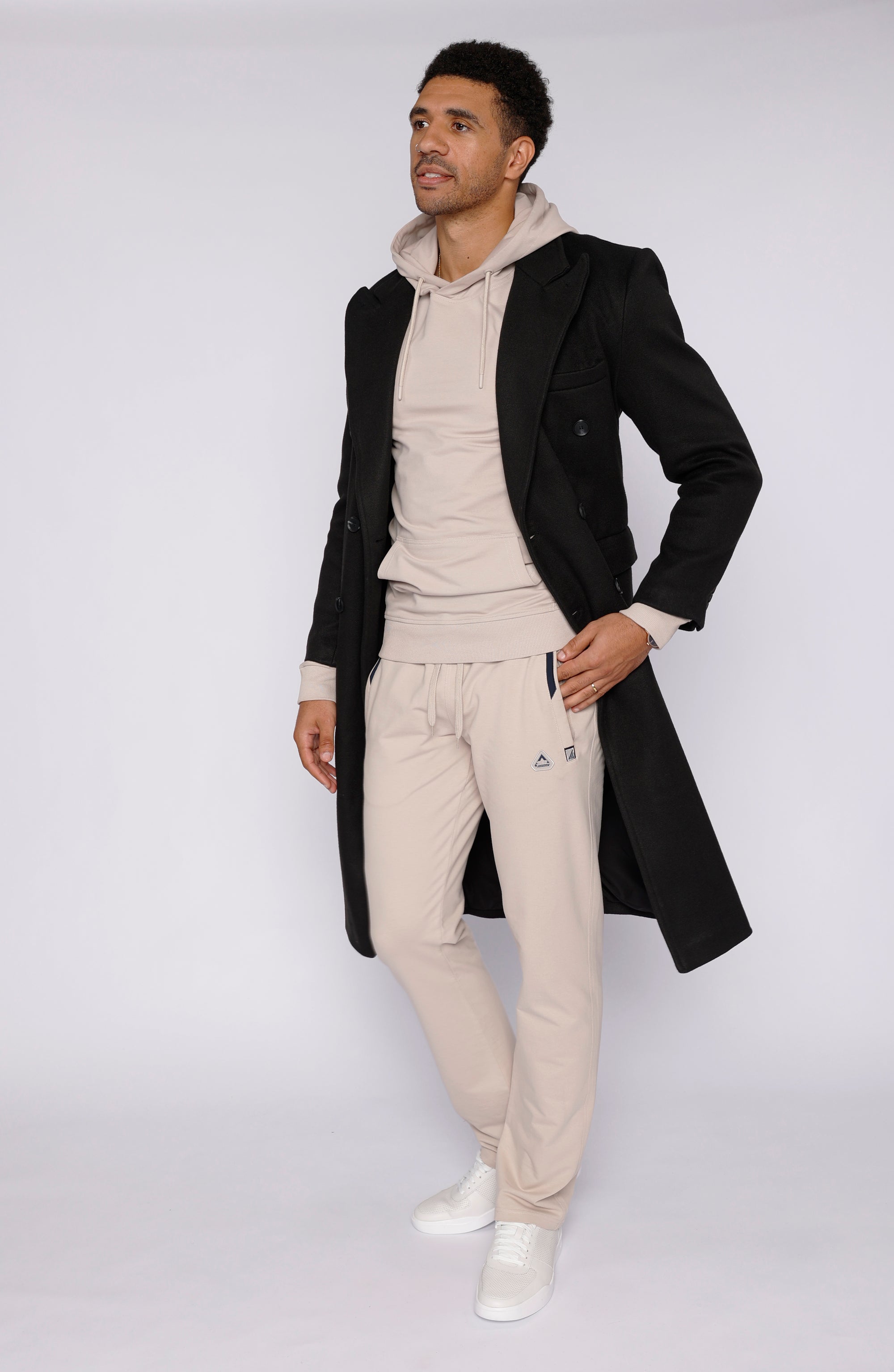 tall male model wearing beige long-inseam sweatpants, beige hoodie and black overcoat, full-body front view