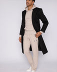 tall male model wearing beige long-inseam sweatpants, beige hoodie and black overcoat, full-body front view