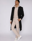 male model wearing beige athletic sweatpants and matching hoodie pared with a long black overcoat, full body lifestyle photos on white background