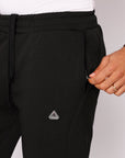 Close up of men's black straight leg athletic pants showing front zipper pocket, drawcord waistband, and SCR Sportswear logo.