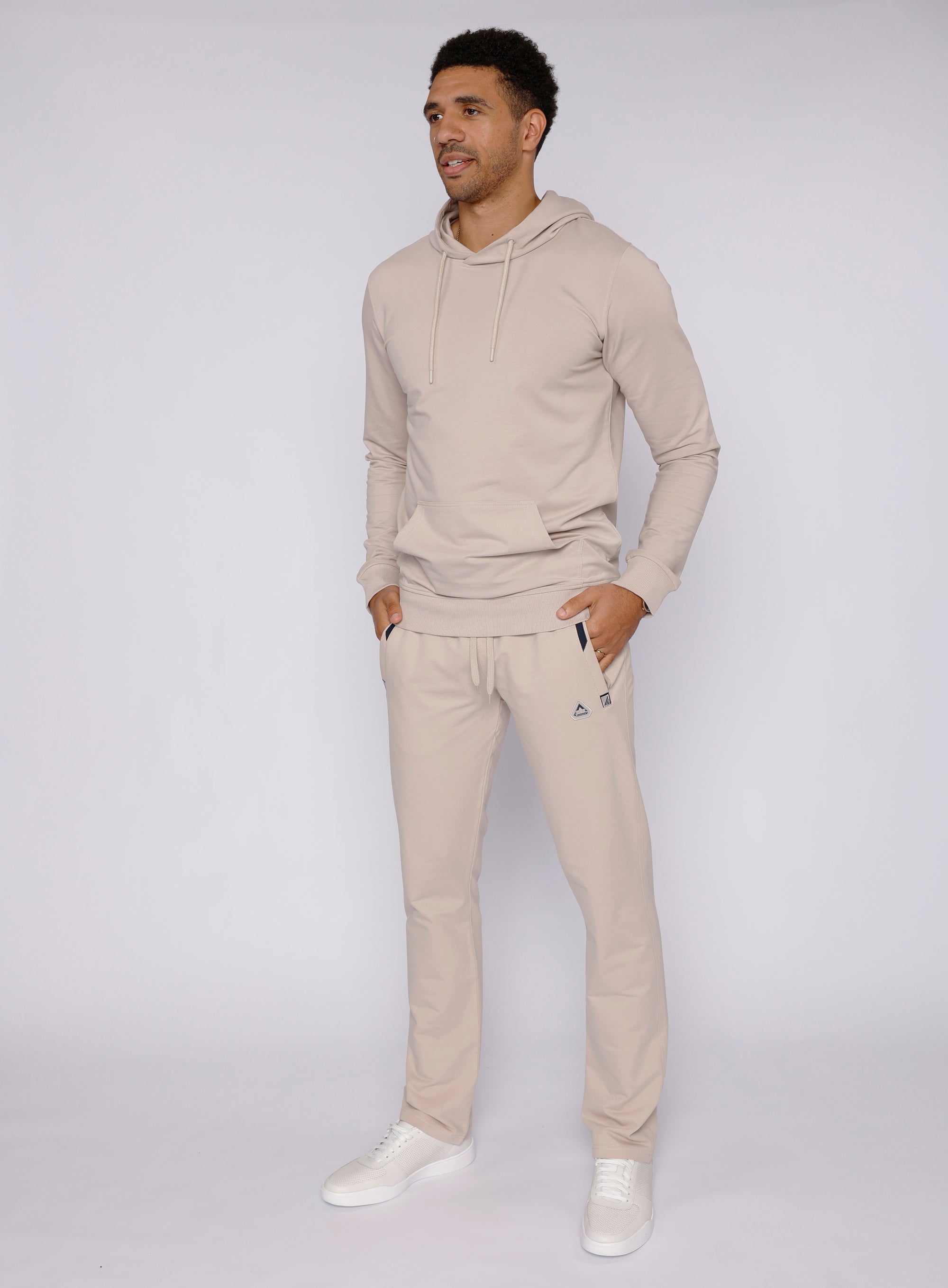 tall male model wearing beige long-inseam sweatpants paired with a beige hoodie, full-body lifestyle view