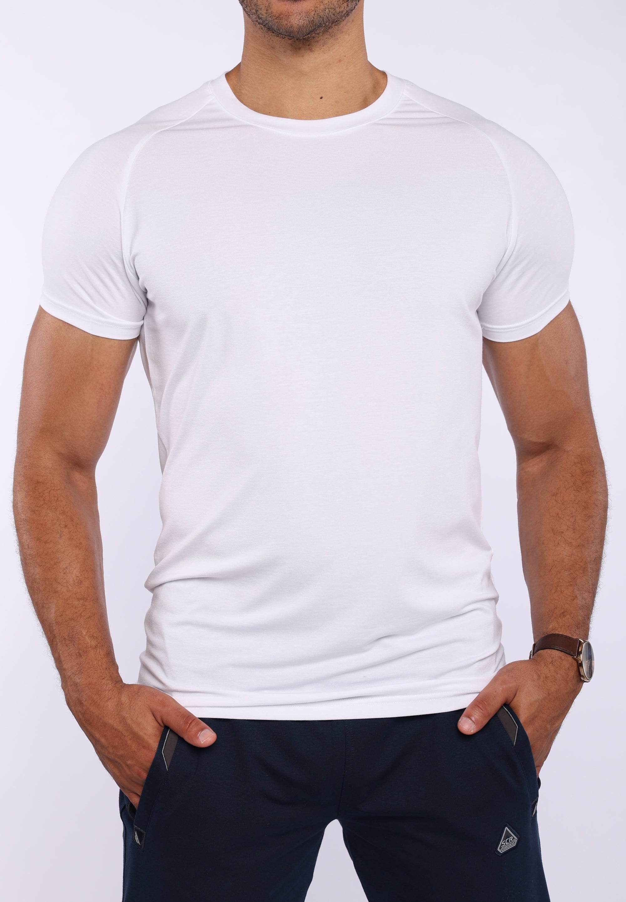 A man wearing a white short-sleeve athletic t-shirt and dark navy pants, standing against a light gray background.