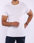 A man wearing a white short-sleeve athletic crewneck t-shirt and dark navy pants, shown from the chin down against a light gray studio background.
