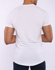 A man viewed from the back wearing a white short-sleeve athletic t-shirt and dark navy pants, set against a plain light gray studio background.