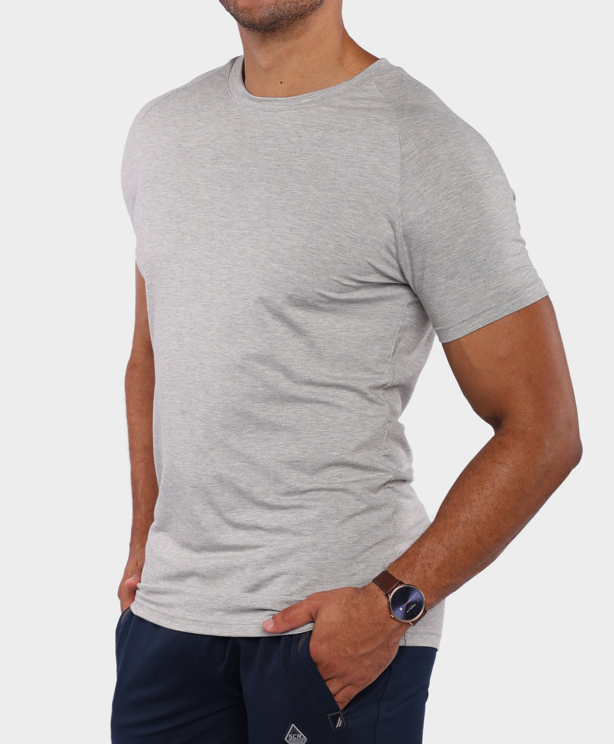 A man wearing a light gray heather crew-neck t-shirt and navy blue pants, shown from the chin down against a light gray background.