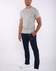 A man modeling a light gray crew-neck t-shirt and navy blue jogger pants with white sneakers, standing against a plain white studio background.