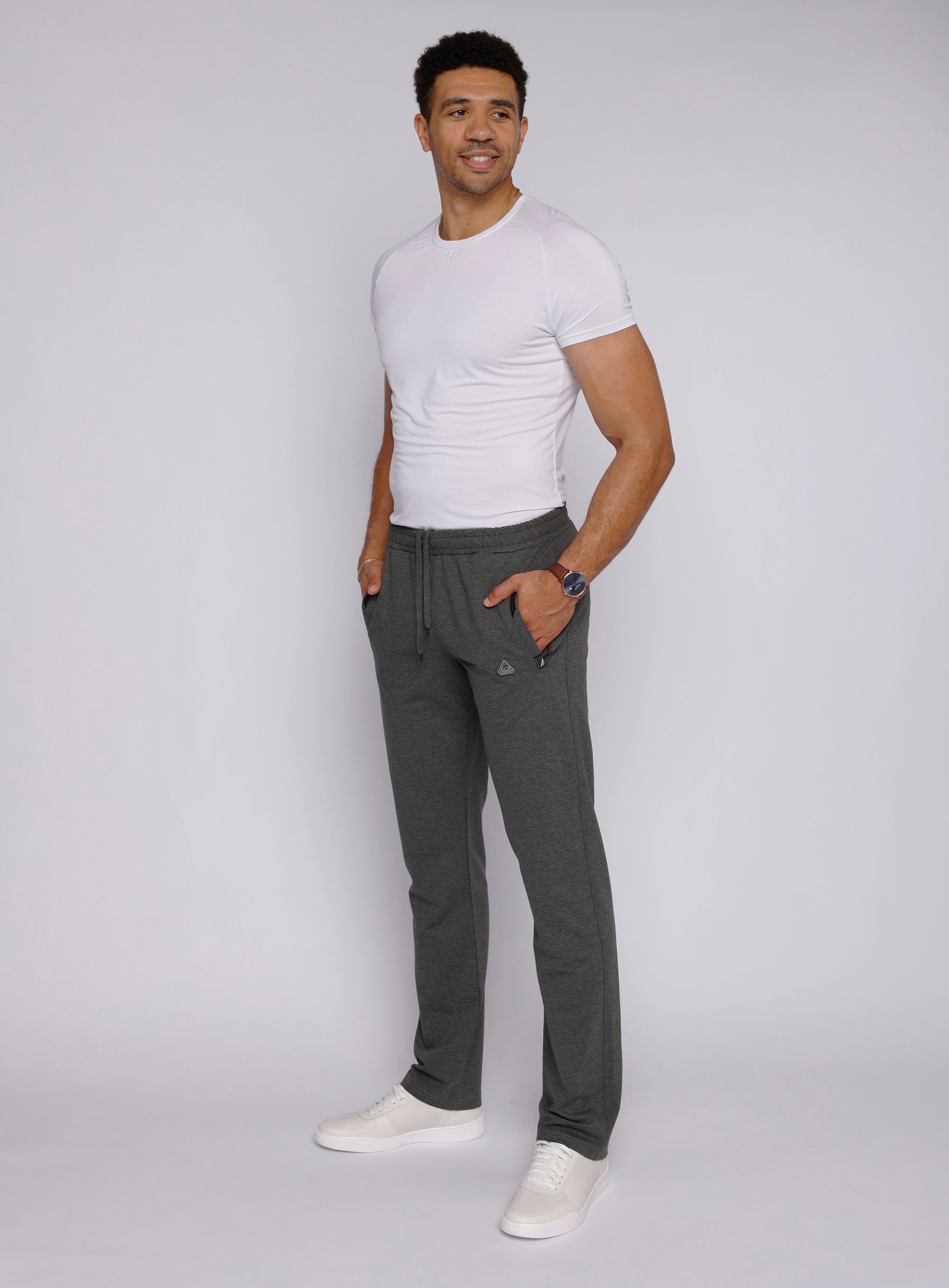 Confident tall male model wearing dark grey 34 inch long inseam athletic sweatpants with zipper pockets, lifestyle view